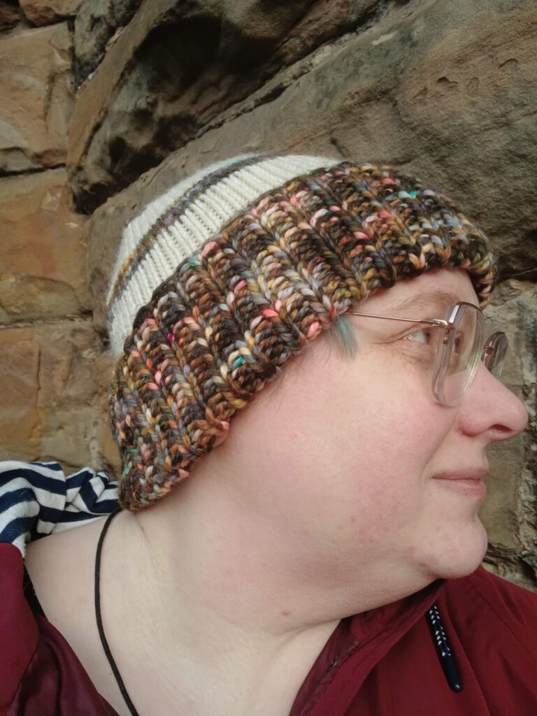 A side view of me wearing the multicoloured Northern Attitude Beanie. You can see the cream stripes on the crown and how the brim covers my ears entirely, keeping me warm and cosy.